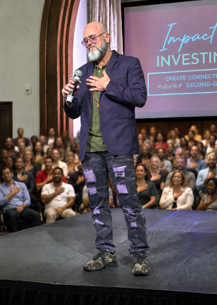 Mark A. Grainger on stage with his hand on his heart in front of a full audience